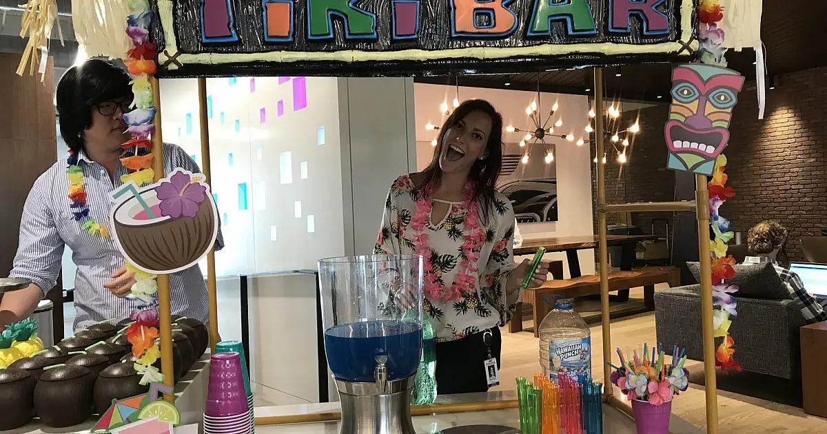 Two employees at a tropical Tiki Bar themed office party with leis and decorations