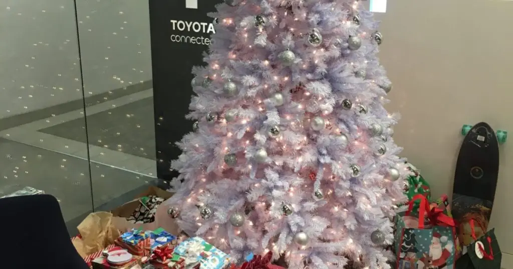 White Christmas tree with silver ornaments and wrapped gifts beneath a Toyota Connected banner