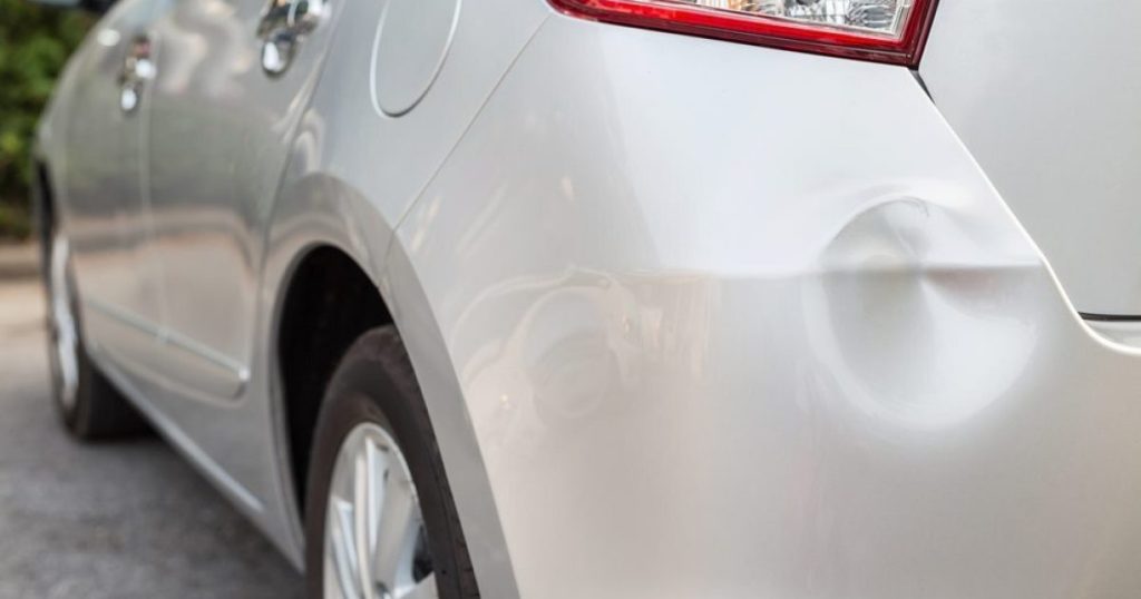 Close-up of a shallow dent in the silver rear body panel of a parked car