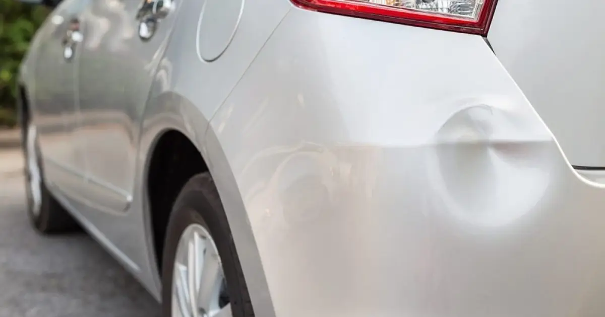 Close-up of a shallow dent in the silver rear body panel of a parked car