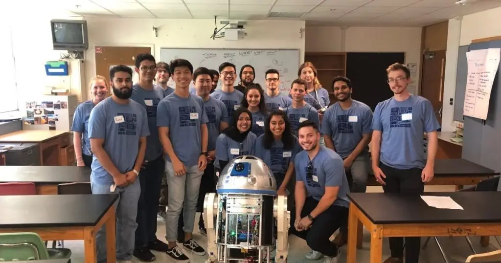 Group of employees in matching blue shirts posing with an R2-D2 robot in a classroom