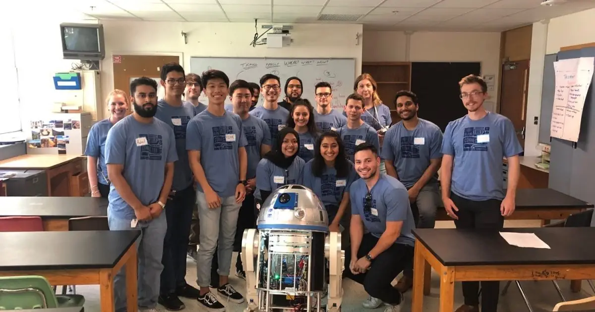 Group of employees in matching blue shirts posing with an R2-D2 robot in a classroom