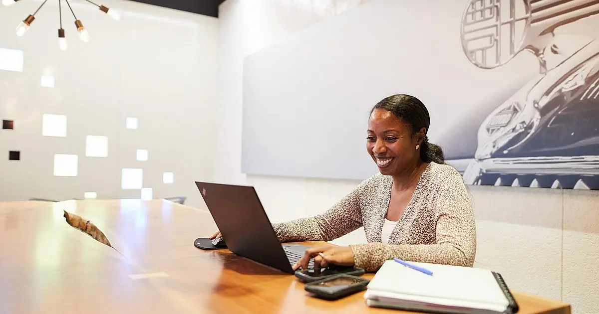 Smiling woman working on a laptop at a wooden table in a modern Toyota Connected office