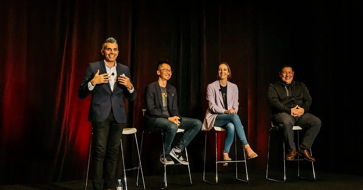Four panelists, one speaking, seated on stools before a red curtain at a company town hall