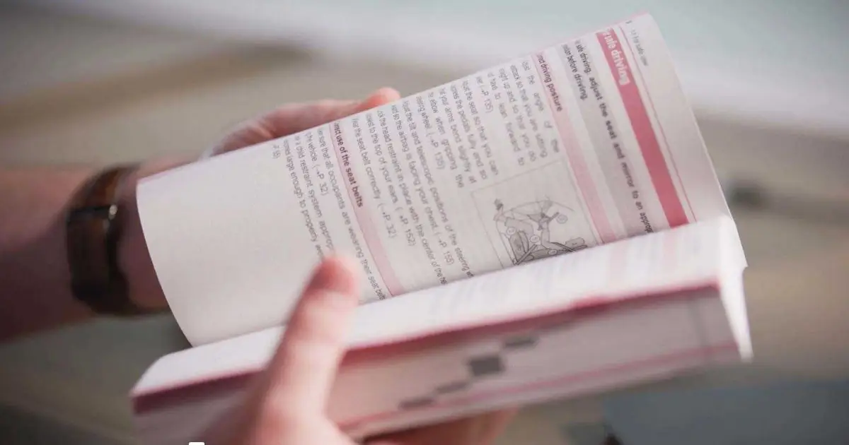 Hands holding an open Toyota owner's manual showing seat and driving posture instructions