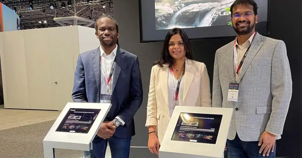 Three colleagues standing beside interactive kiosks at a Lexus auto show display