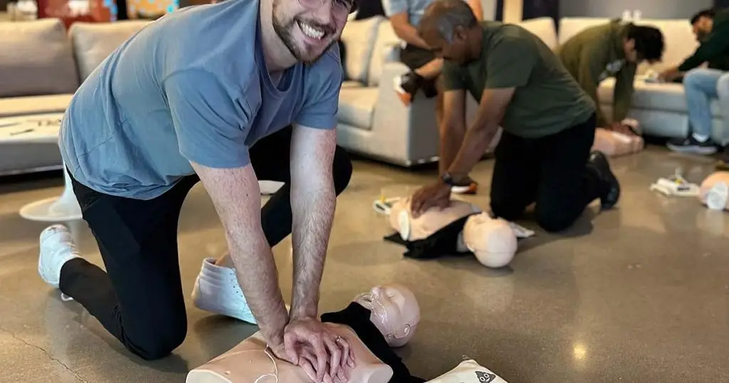 Smiling man practicing chest compressions on a CPR manikin during a training session