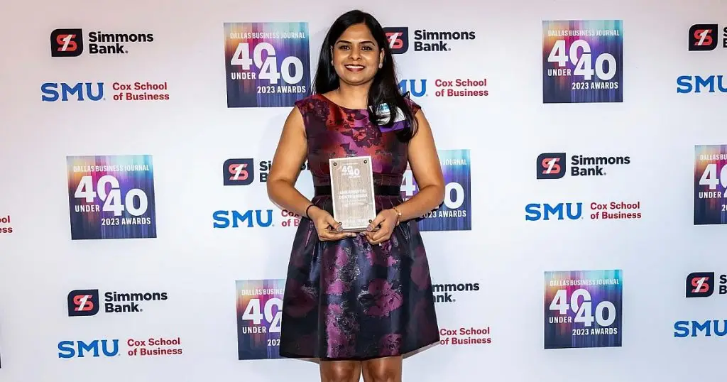 Woman holding a glass award in front of a Dallas Business Journal 40 Under 40 backdrop