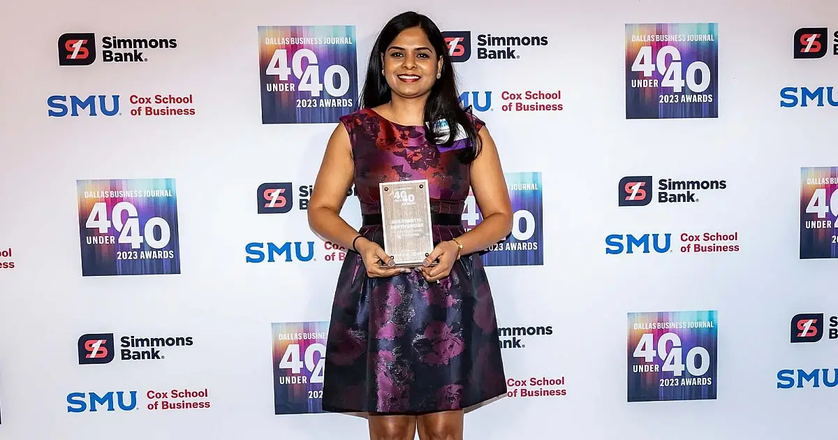 Woman holding a glass award in front of a Dallas Business Journal 40 Under 40 backdrop