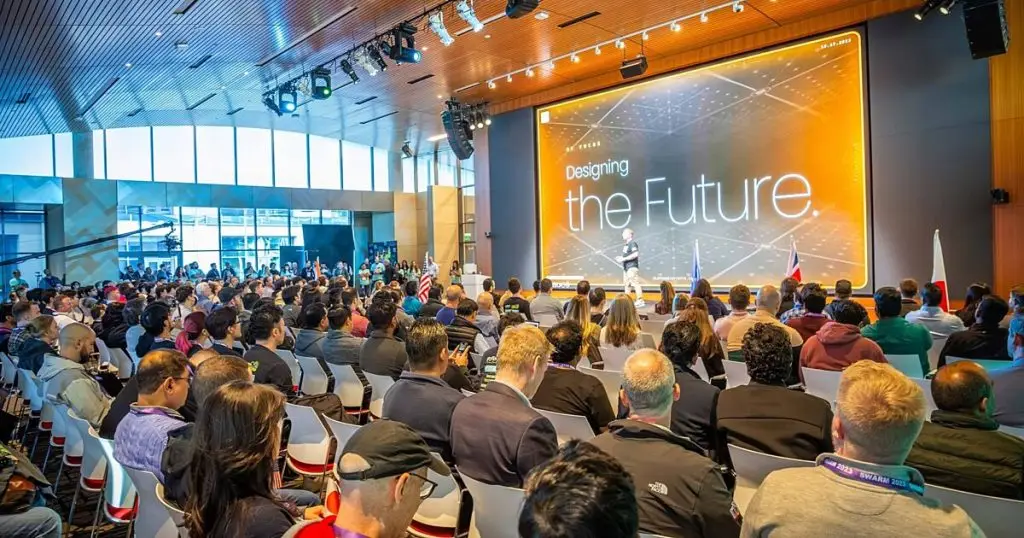 Audience seated facing a large stage screen reading Designing the Future at a conference