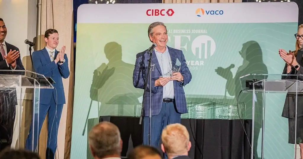 Man smiling on stage holding a glass award as others applaud at a CFO awards event