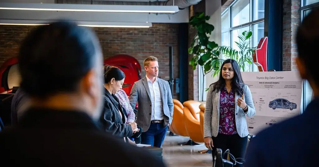 Woman presenting to colleagues beside a Toyota Big Data Center poster in the office