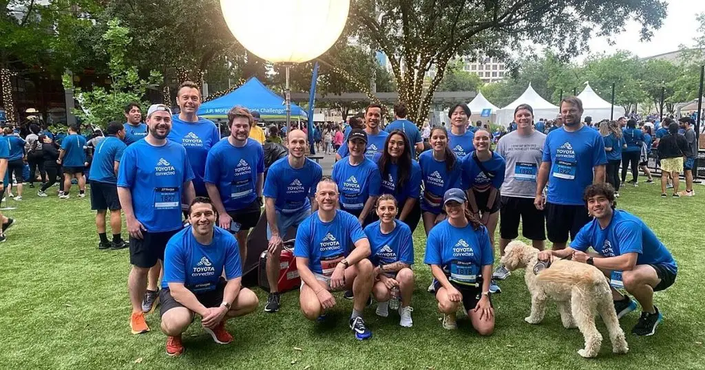 Team in matching blue Toyota Connected shirts posing at an outdoor running event with a dog