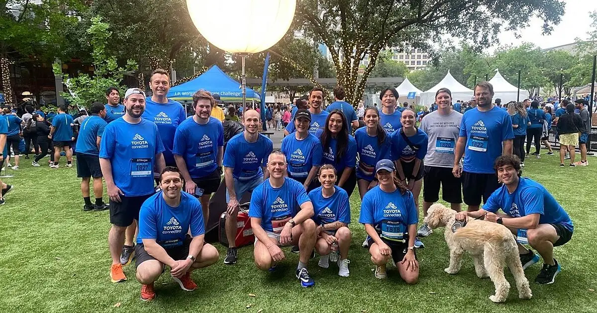 Team in matching blue Toyota Connected shirts posing at an outdoor running event with a dog