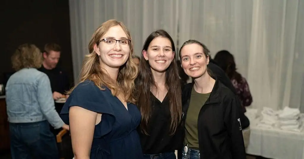 Three women smiling together at an evening networking event