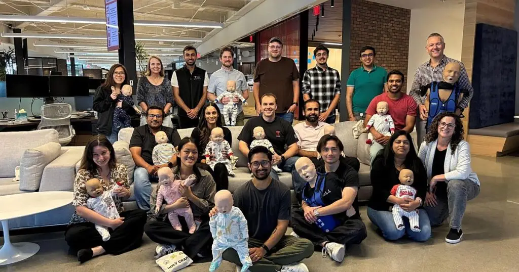Large group of employees holding infant CPR training manikins in the office