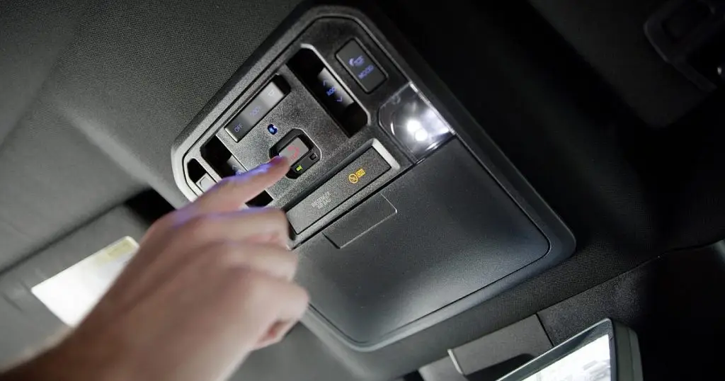 Finger pressing the SOS emergency call button on a car's overhead console