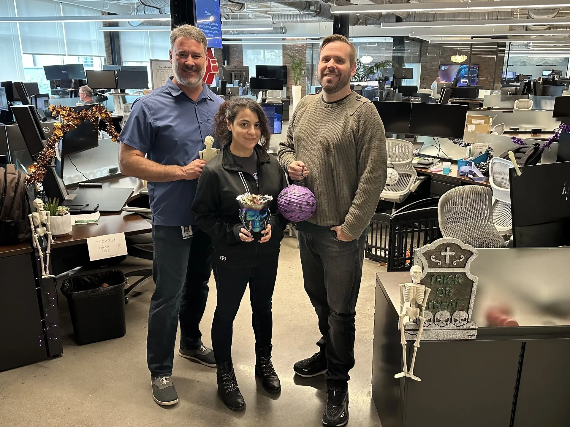 Three coworkers posing with Halloween decorations and skeletons in the open office