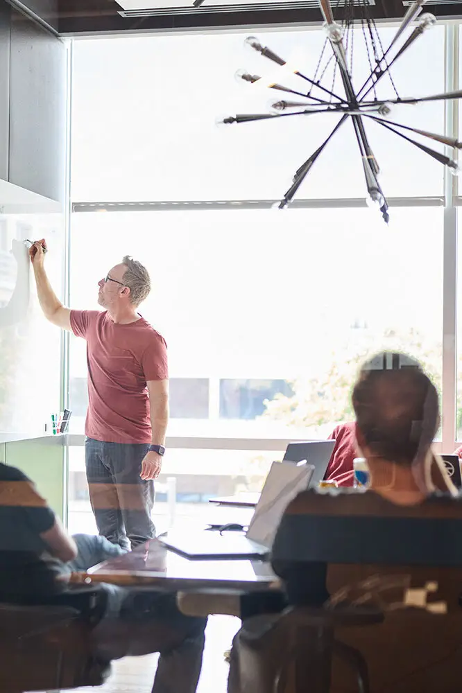 Man writing on a whiteboard during a meeting in a sunlit conference room