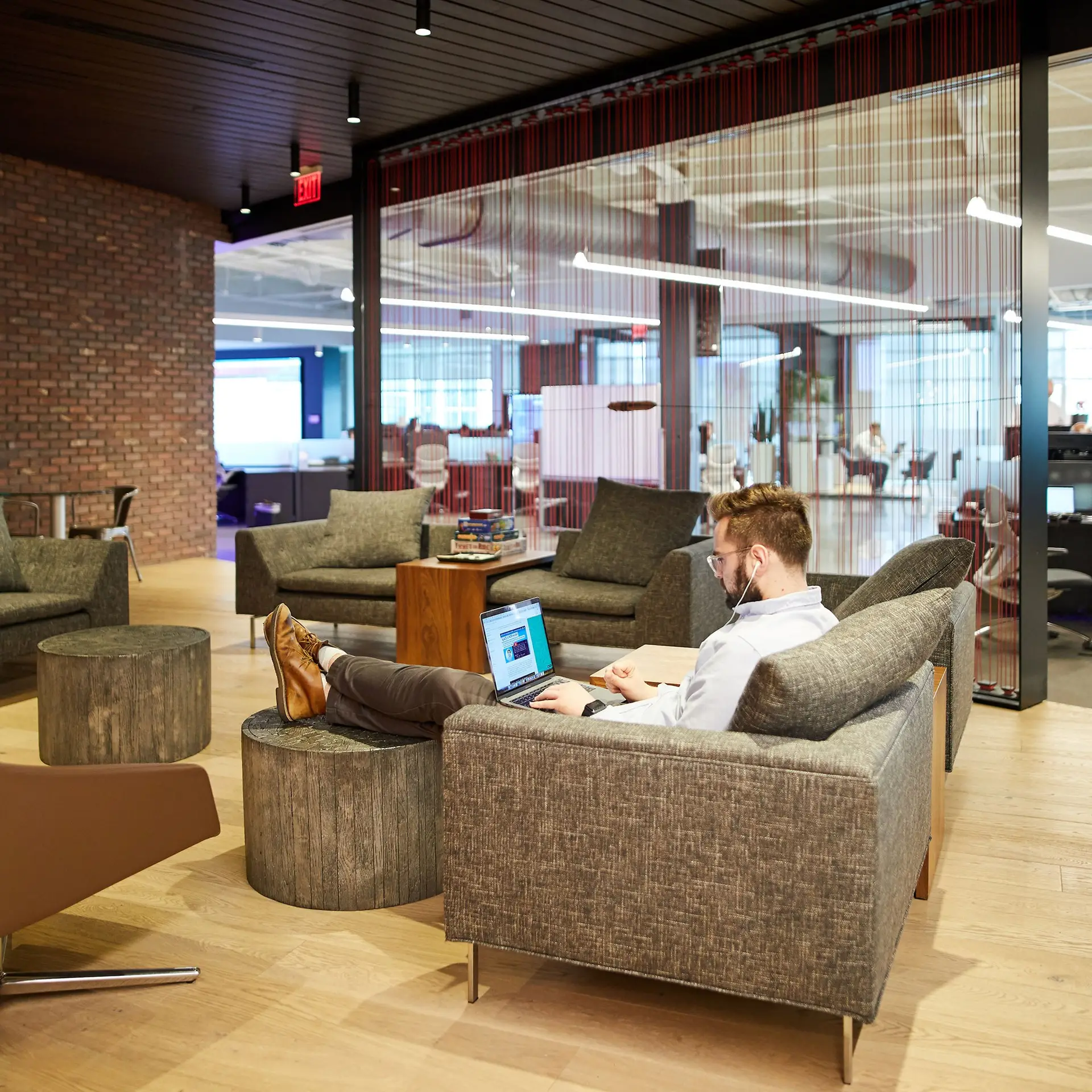 Employee works on a laptop in a relaxed office lounge with sofas and glass walls