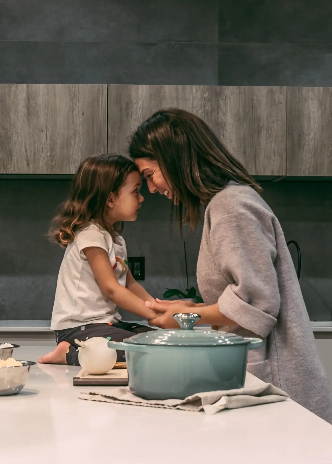 Smiling woman and her young child touching foreheads while cooking in a kitchen