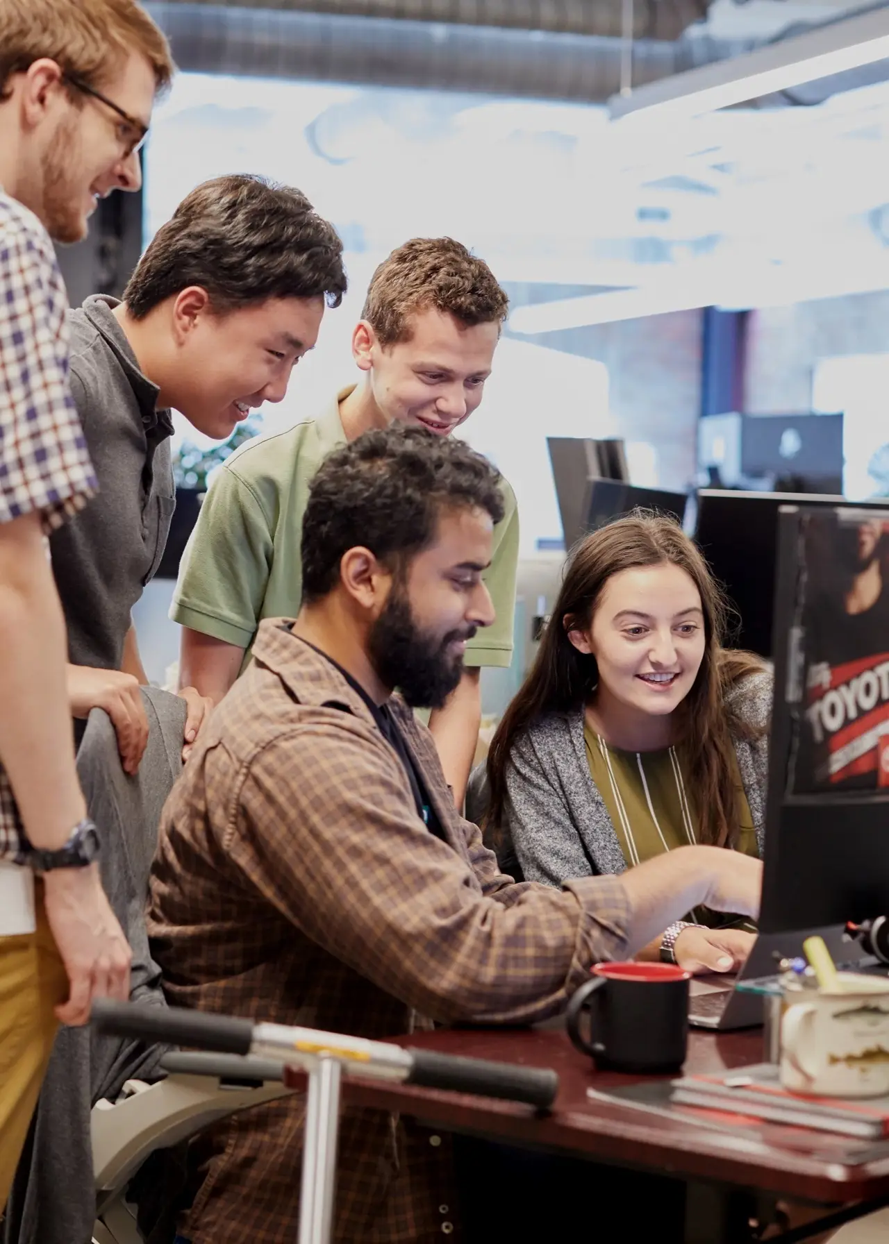 Five colleagues gathered around a monitor, smiling as one points at the screen